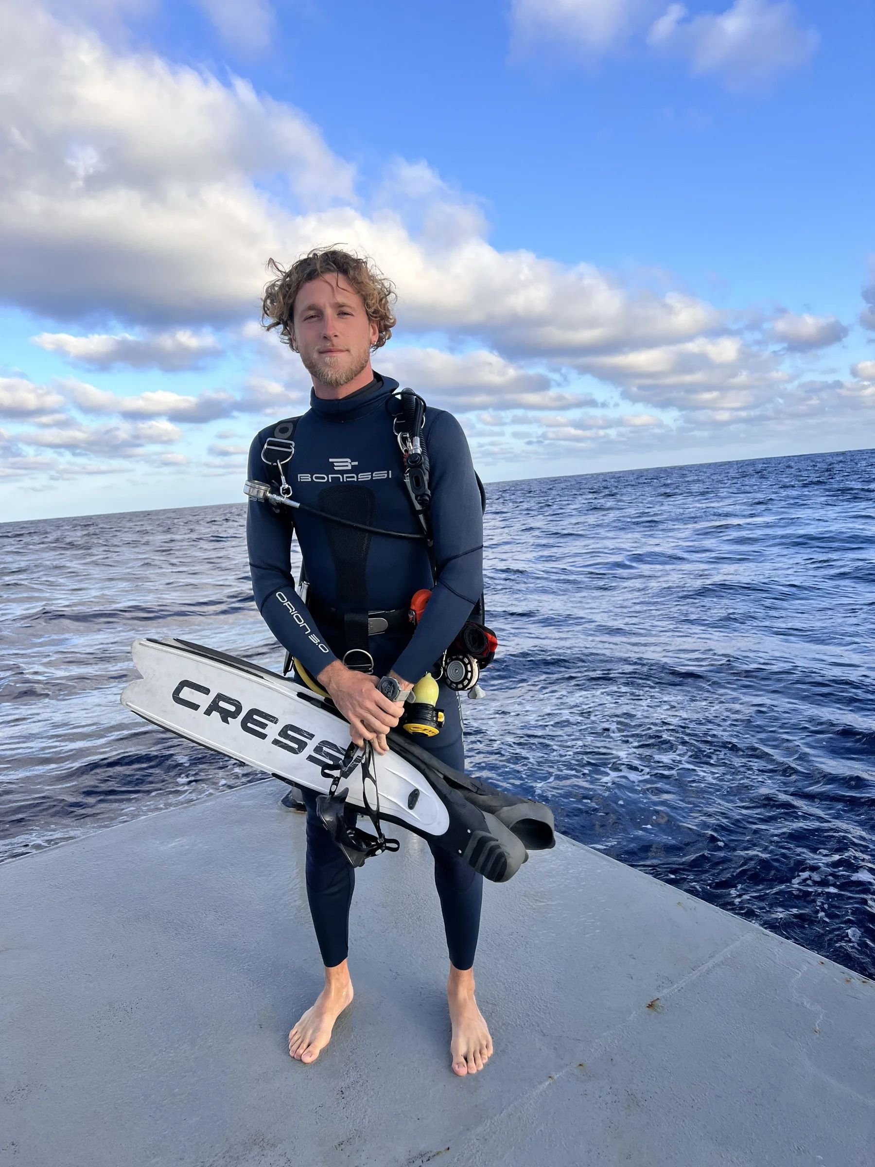 Dani in a wetsuit on the bow with his fins, open ocean behind